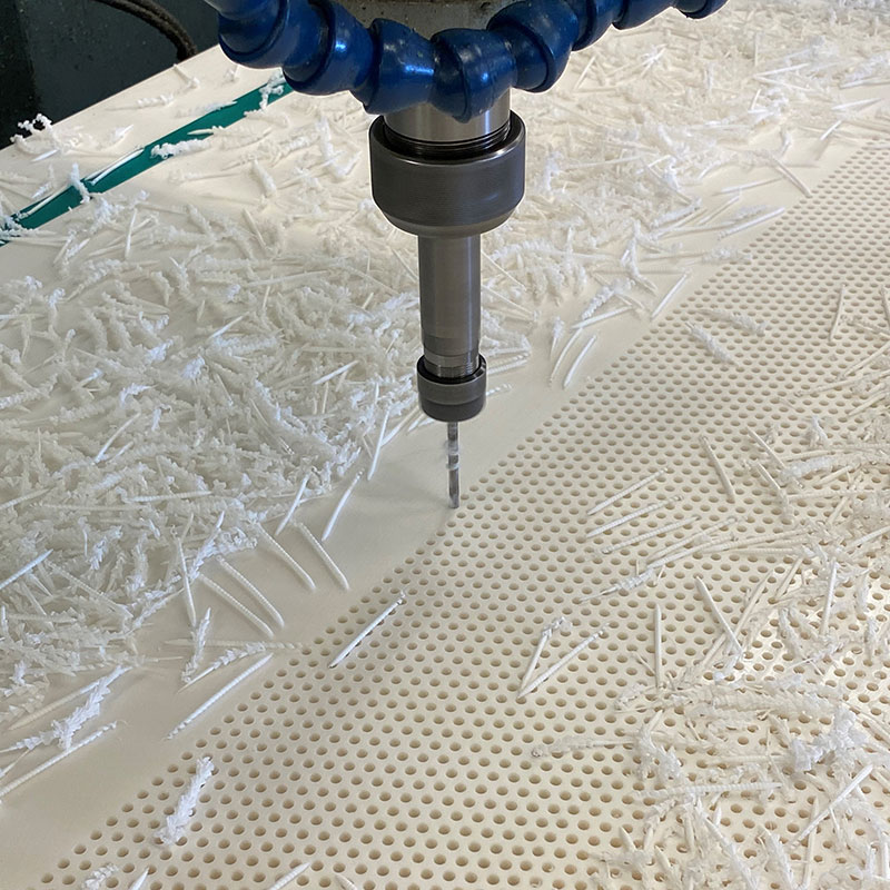 CNC Machining tool creating a perforated panel from white plastic