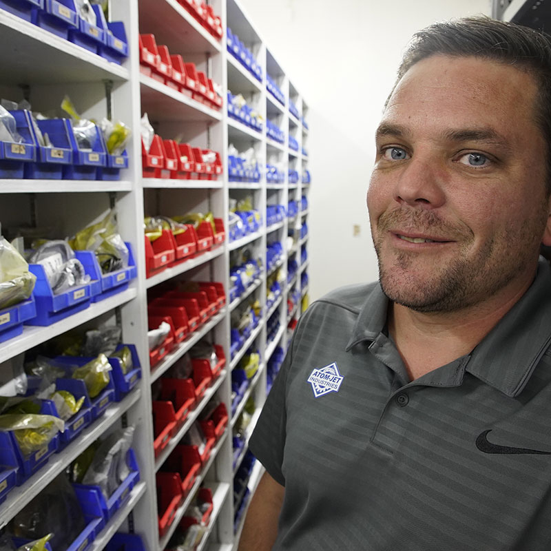 Atom-Jet employee standing near shelves containing parts.